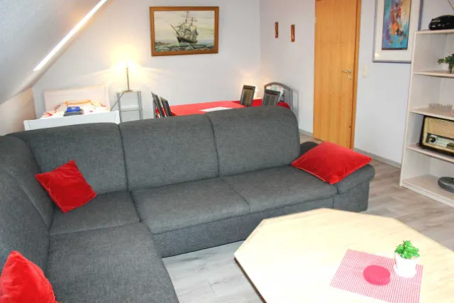 Wohnraum mit grauem Ecksofa und roten Kissen